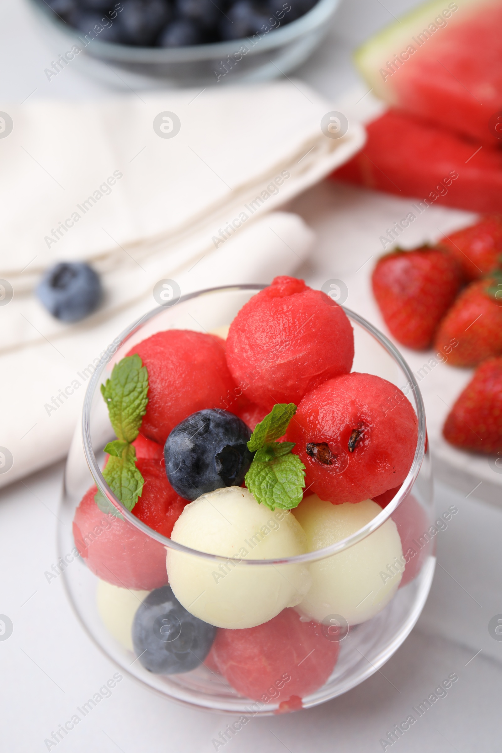 Photo of Tasty watermelon and melon balls with blueberries in glass on white table, closeup