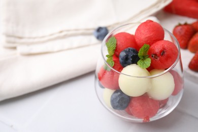 Photo of Tasty watermelon and melon balls with blueberries in glass on white tiled table, closeup. Space for text