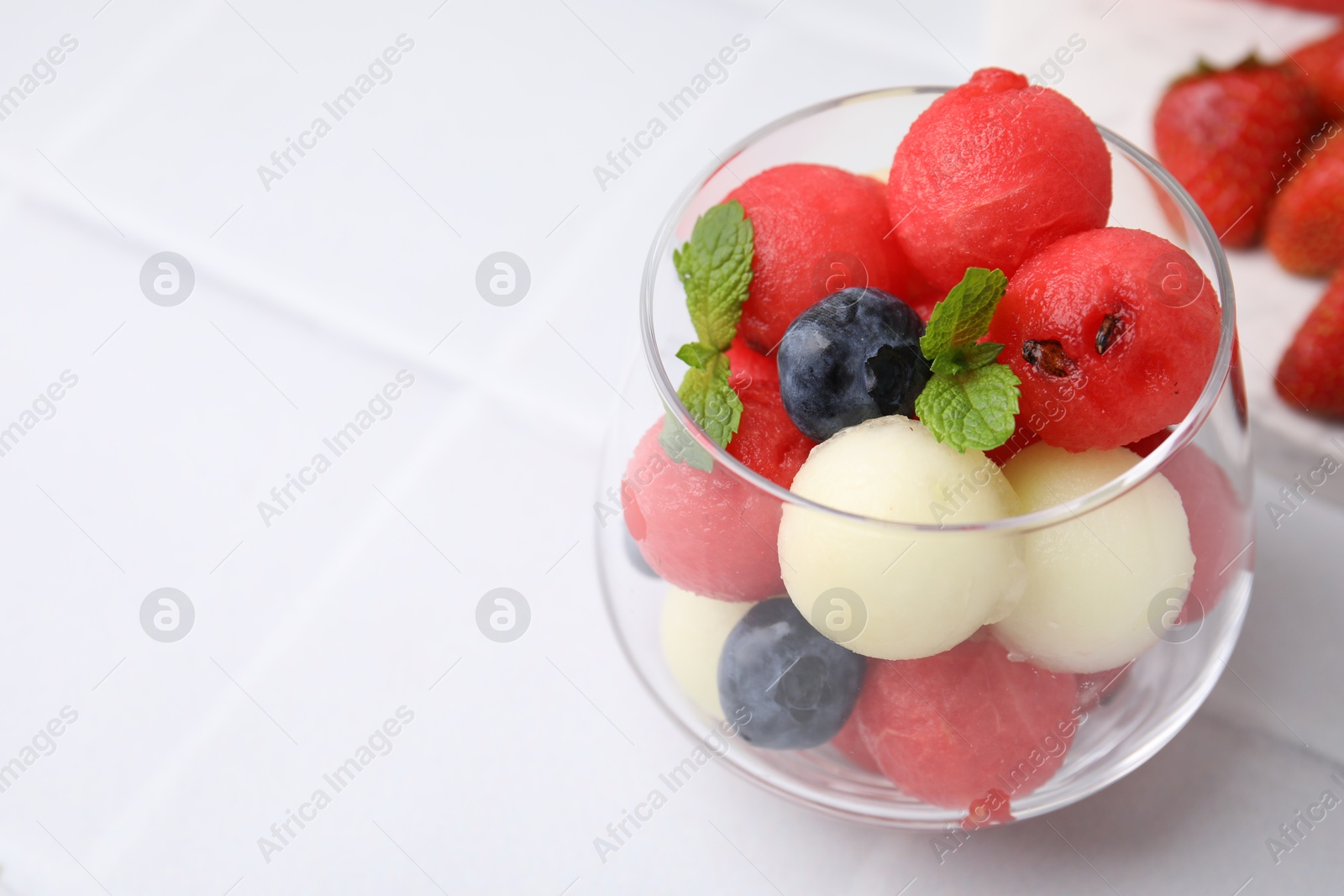 Photo of Tasty watermelon and melon balls with blueberries in glass on white tiled table, closeup. Space for text