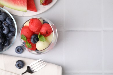 Photo of Tasty watermelon and melon balls with blueberries in glass on white tiled table, flat lay. Space for text