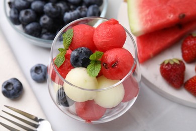 Photo of Tasty watermelon and melon balls with blueberries in glass on white table, closeup