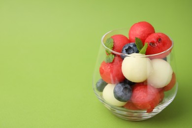 Photo of Tasty watermelon and melon balls with blueberries in glass on green table, closeup. Space for text