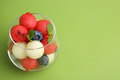 Tasty watermelon and melon balls with blueberries in glass on green table, closeup. Space for text