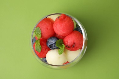 Tasty watermelon and melon balls with blueberries in glass on green table, top view