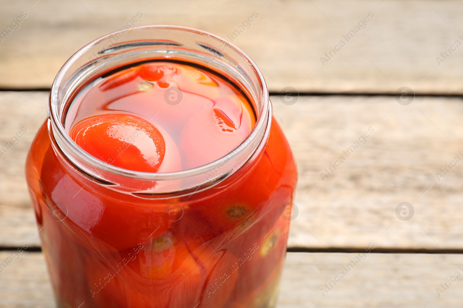 Photo of Tasty pickled tomatoes in jar on wooden table, closeup. Space for text