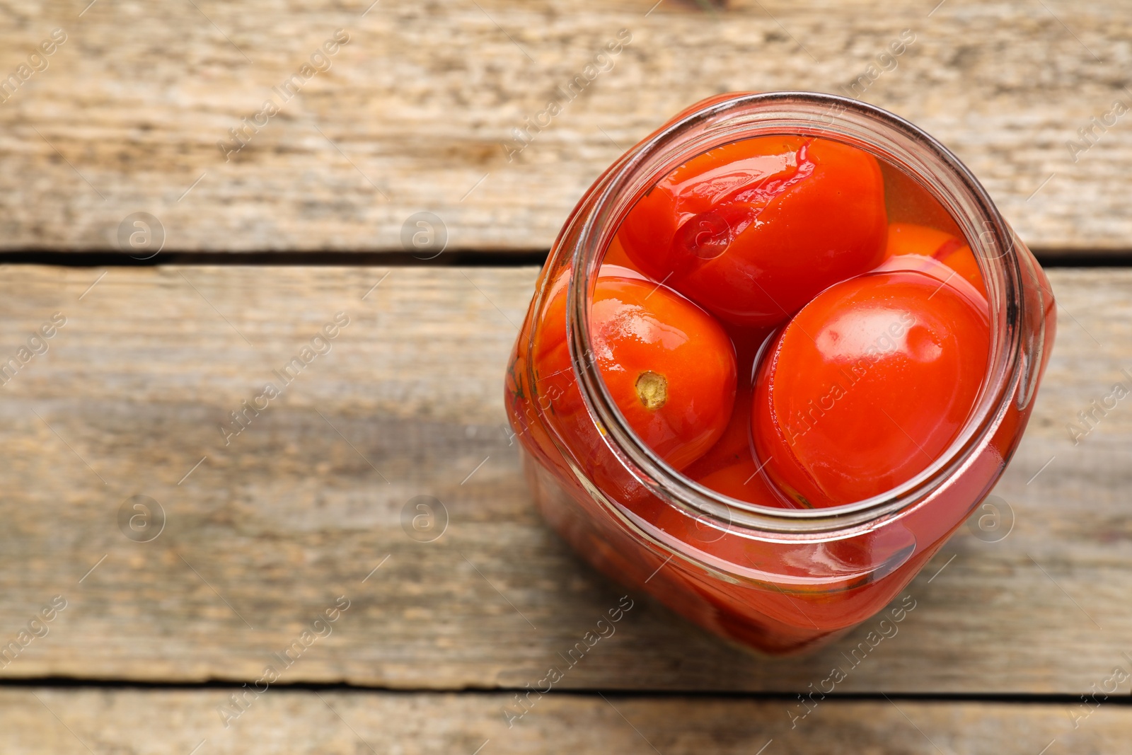 Photo of Tasty pickled tomatoes in jar on wooden table, top view. Space for text