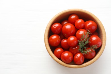 Tasty pickled tomatoes and dill in bowl on white wooden table, top view. Space for text