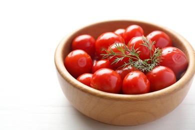 Photo of Tasty pickled tomatoes and dill in bowl on white wooden table, closeup. Space for text