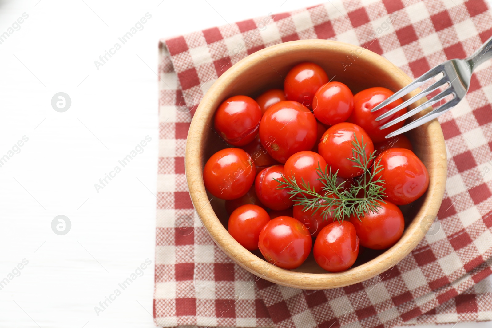 Photo of Tasty pickled tomatoes in bowl, dill and fork on white table, top view. Space for text