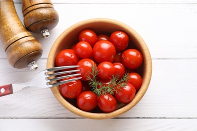 Photo of Tasty pickled tomatoes in bowl, dill and fork on white wooden table, top view