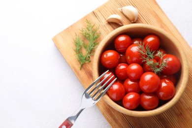 Tasty pickled tomatoes, dill, garlic and fork on white table, top view. Space for text