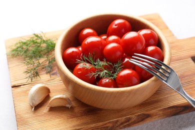 Photo of Tasty pickled tomatoes in bowl, dill, garlic and fork on table