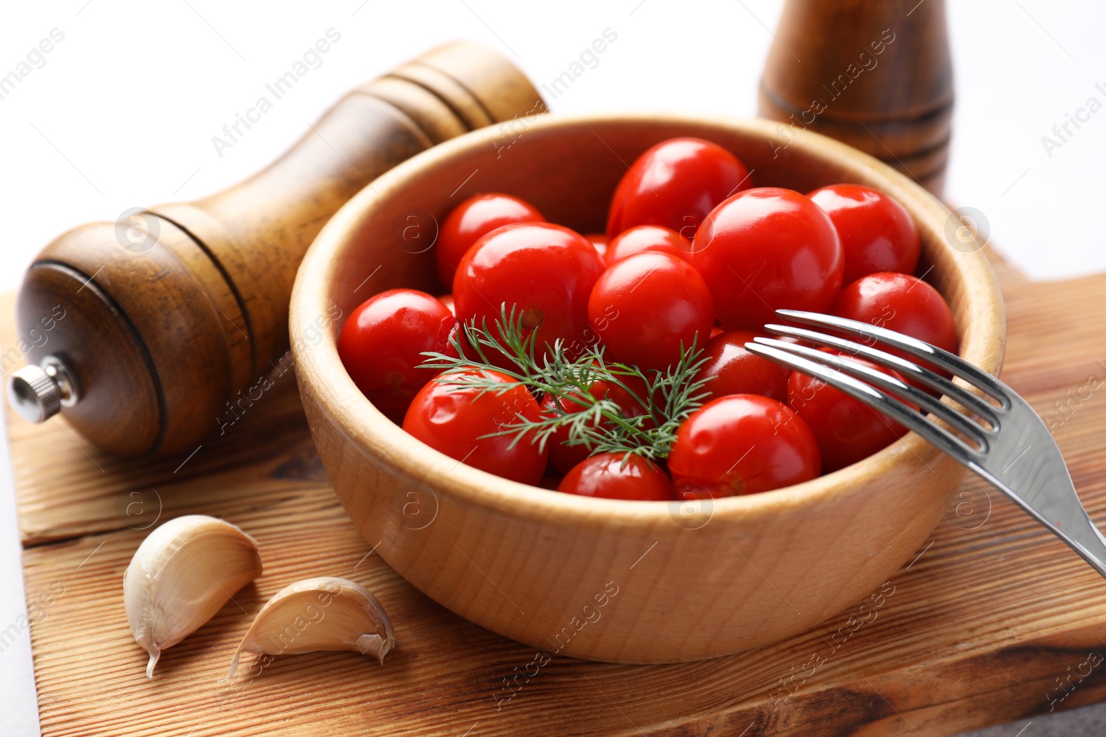 Photo of Tasty pickled tomatoes in bowl, dill, garlic and fork on table, closeup