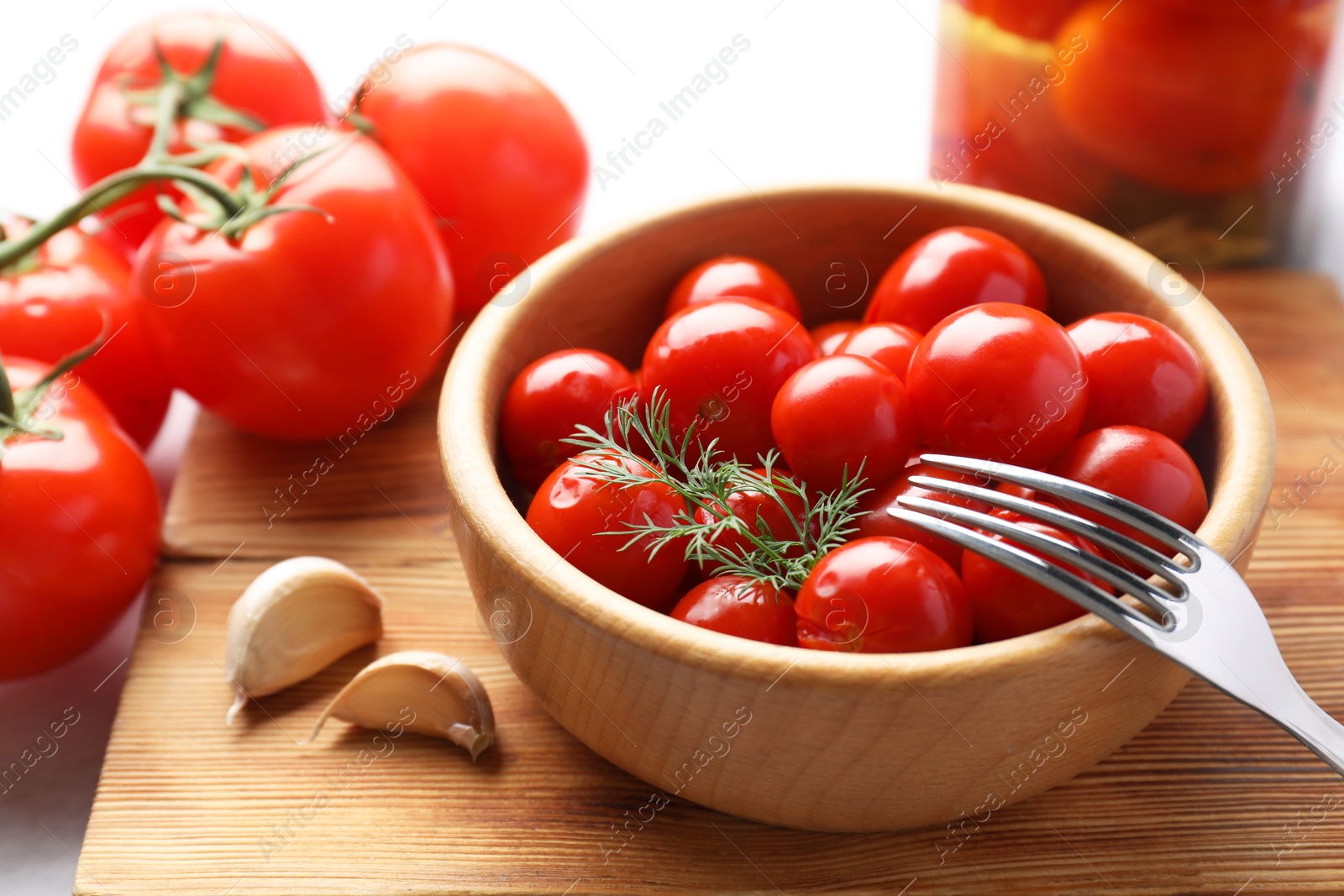 Photo of Tasty pickled tomatoes in bowl, fresh vegetables, dill, garlic and fork on table