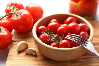 Photo of Tasty pickled tomatoes in bowl, fresh vegetables, dill, garlic and fork on table