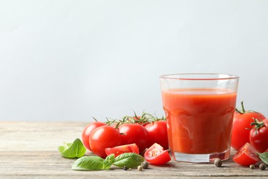 Photo of Tasty tomato juice in glass with fresh vegetables and spices on wooden table, space for text