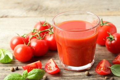 Photo of Tasty tomato juice in glass with fresh vegetables and spices on wooden table, closeup