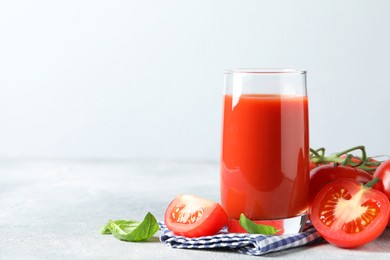 Tasty tomato juice in glass with fresh vegetables and basil leaves on light grey table, space for text