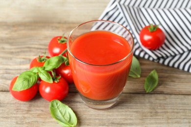 Photo of Tasty tomato juice in glass, basil leaves and fresh vegetables on wooden table