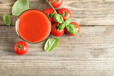 Photo of Tasty tomato juice in glass, basil leaves and fresh vegetables on wooden table, flat lay. Space for text