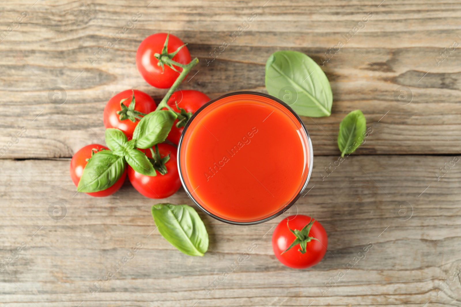 Photo of Tasty tomato juice in glass, basil leaves and fresh vegetables on wooden table, flat lay