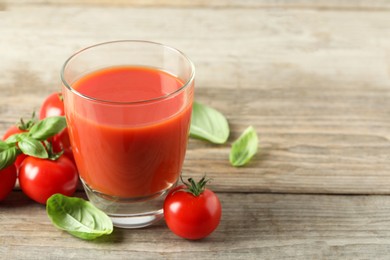 Photo of Tasty tomato juice in glass, basil leaves and fresh vegetables on wooden table, space for text