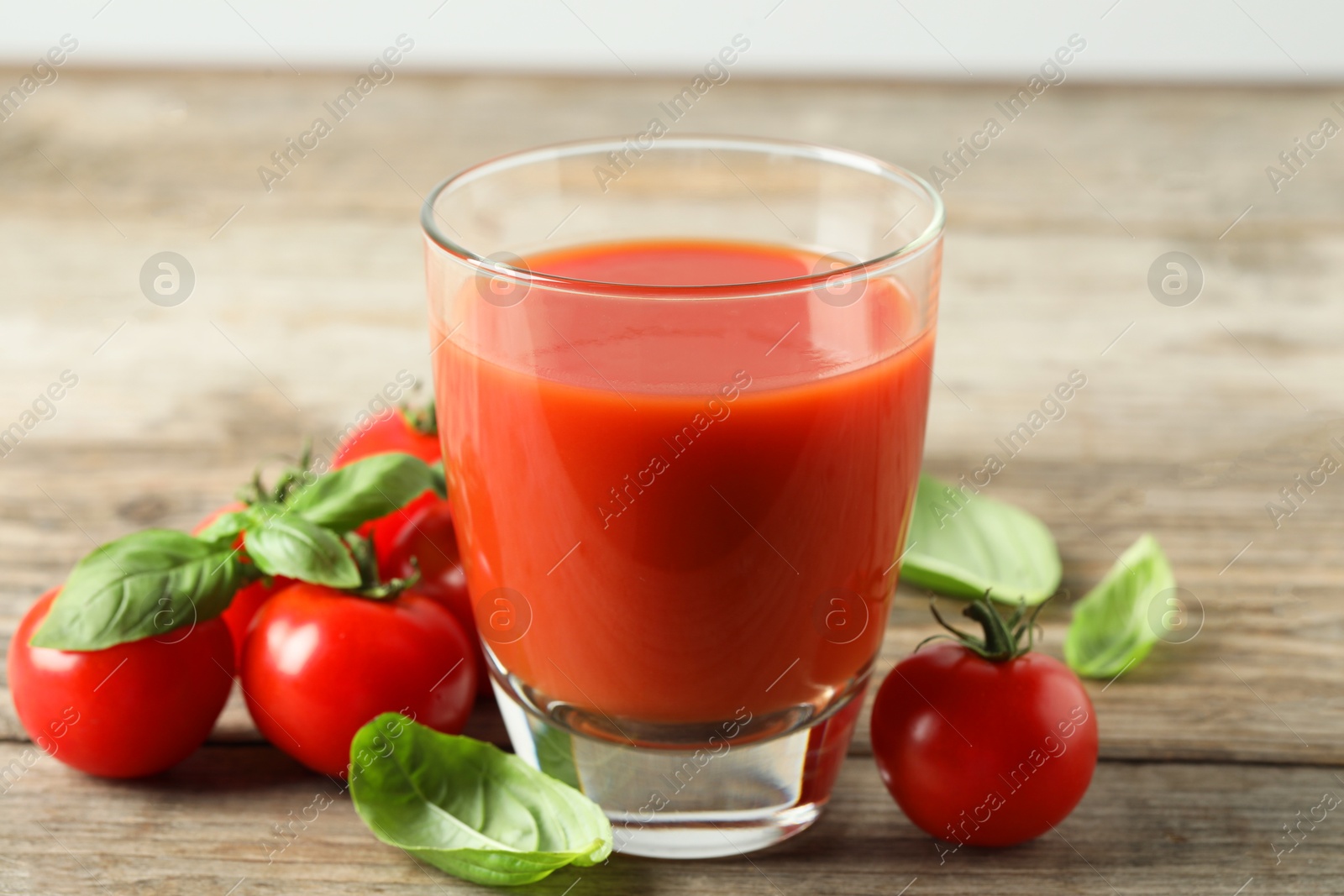 Photo of Tasty tomato juice in glass, basil leaves and fresh vegetables on wooden table, closeup