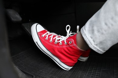 Photo of Woman in sneakers pushing on pedal of car brake, closeup