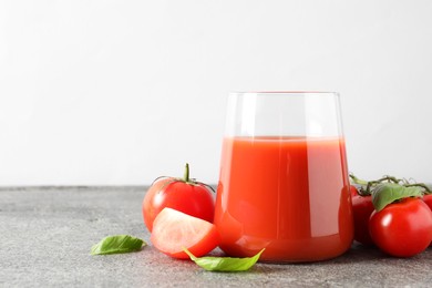 Photo of Tasty tomato juice in glass, basil and fresh vegetables on grey table. Space for text