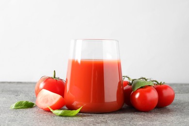 Tasty tomato juice in glass, basil and fresh vegetables on grey table