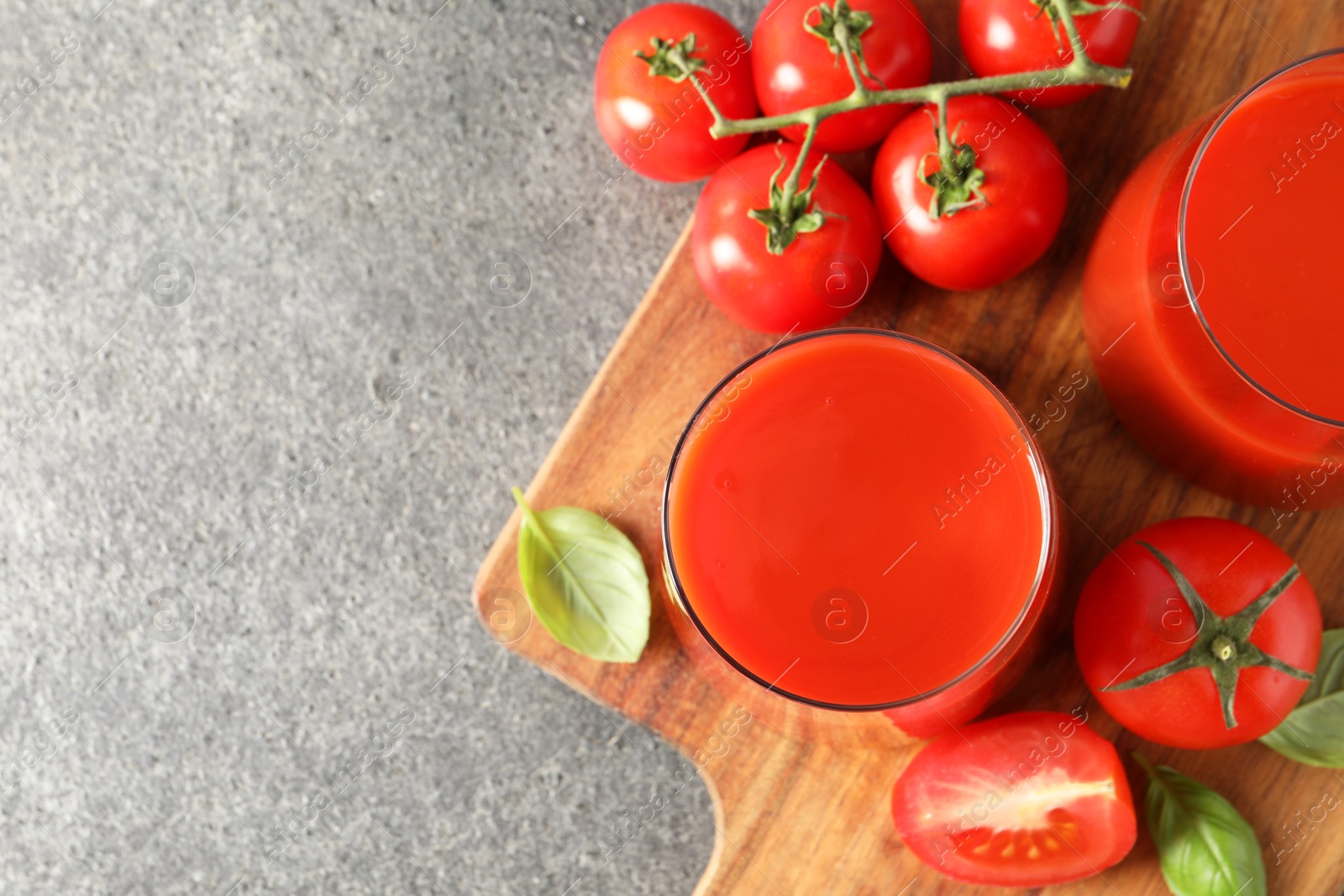 Photo of Tasty tomato juice in glasses, basil and fresh vegetables on grey table, top view. Space for text