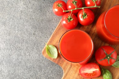 Tasty tomato juice in glasses, basil and fresh vegetables on grey table, top view. Space for text