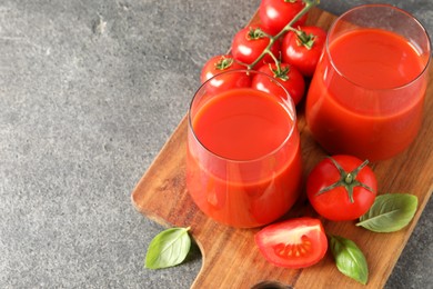 Photo of Tasty tomato juice in glasses, basil and fresh vegetables on grey table, space for text