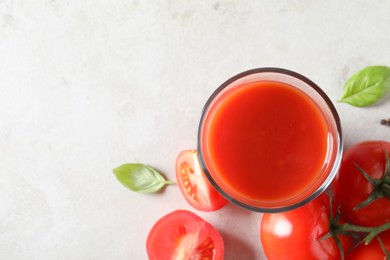 Photo of Tasty tomato juice in glass, basil leaves and fresh vegetables on light grey table, top view. Space for text