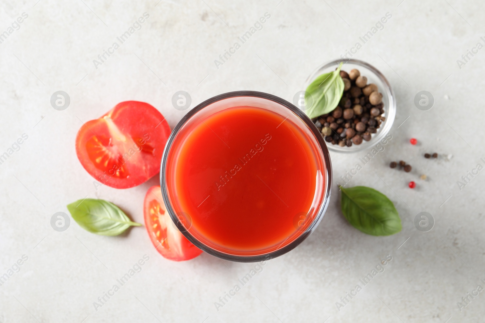 Photo of Tasty tomato juice in glass, basil leaves, peppercorns and fresh vegetables on light grey table, flat lay