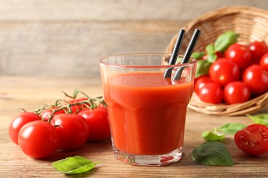 Photo of Tasty tomato juice in glass, basil leaves and fresh vegetables on wooden table