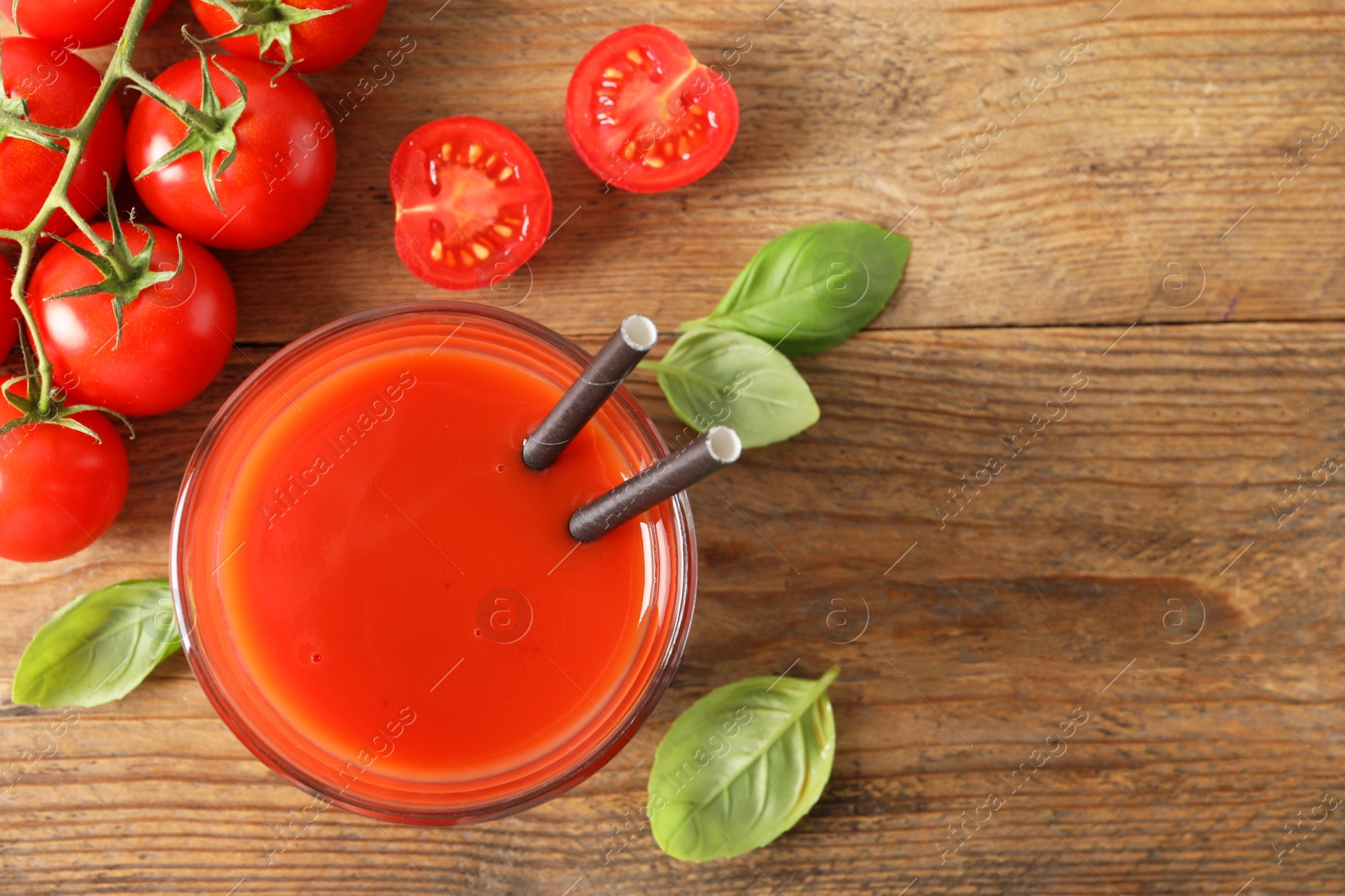 Photo of Tasty tomato juice in glass, basil leaves and fresh vegetables on wooden table, flat lay. Space for text