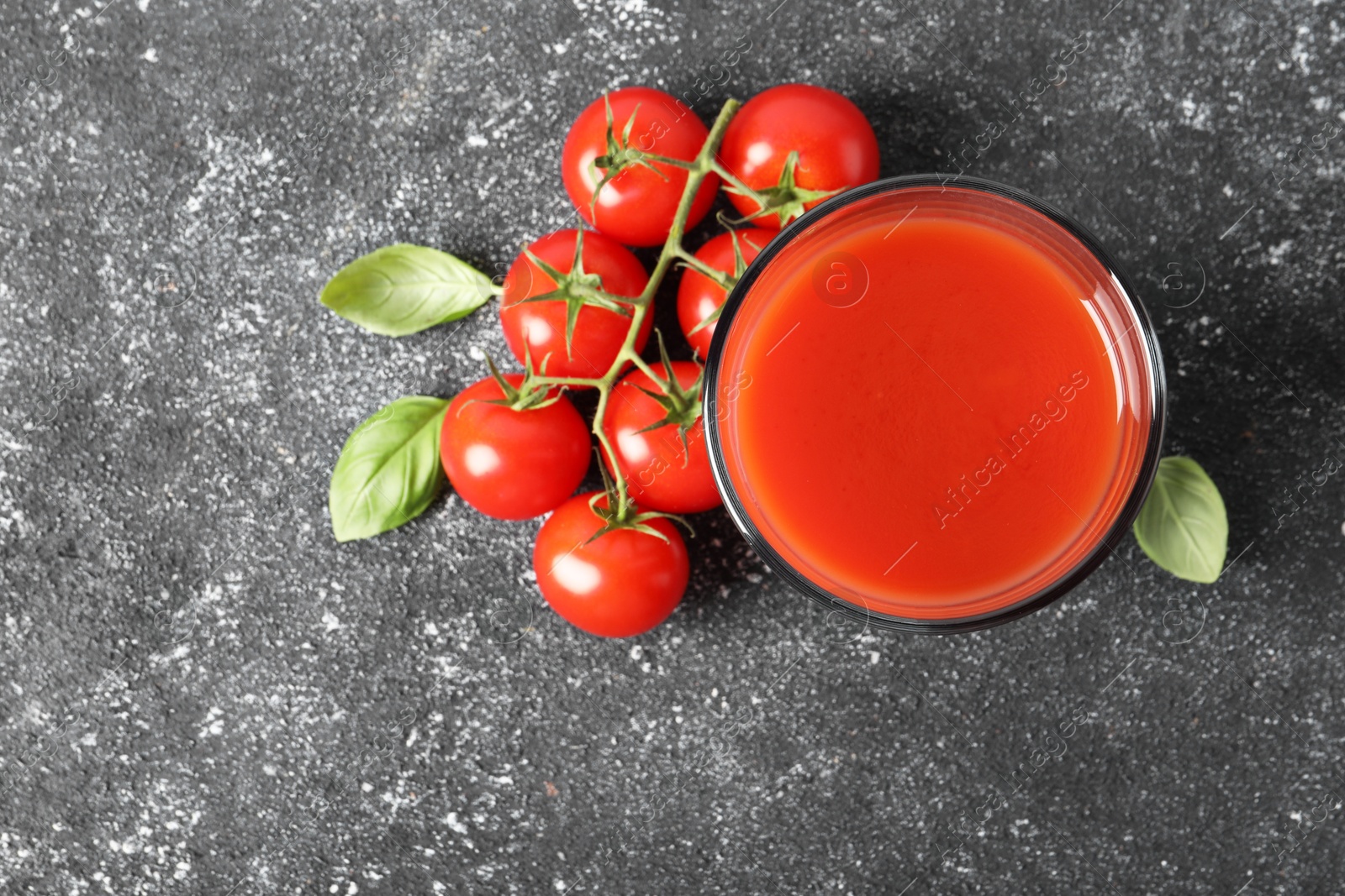 Photo of Tasty tomato juice in glass, basil and fresh vegetables on grey table, top view