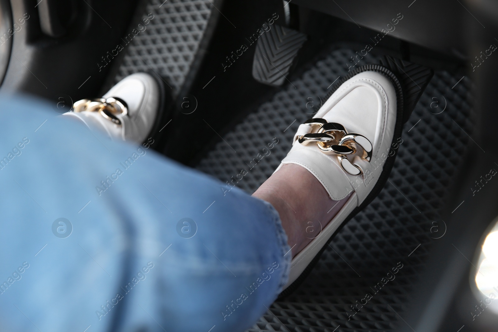 Photo of Woman in white shoes pushing on pedal of car brake, closeup