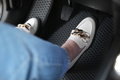 Woman in white shoes pushing on pedal of car brake, closeup