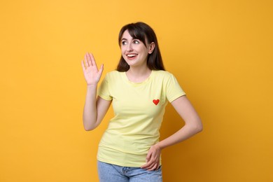 Happy young woman waving on orange background