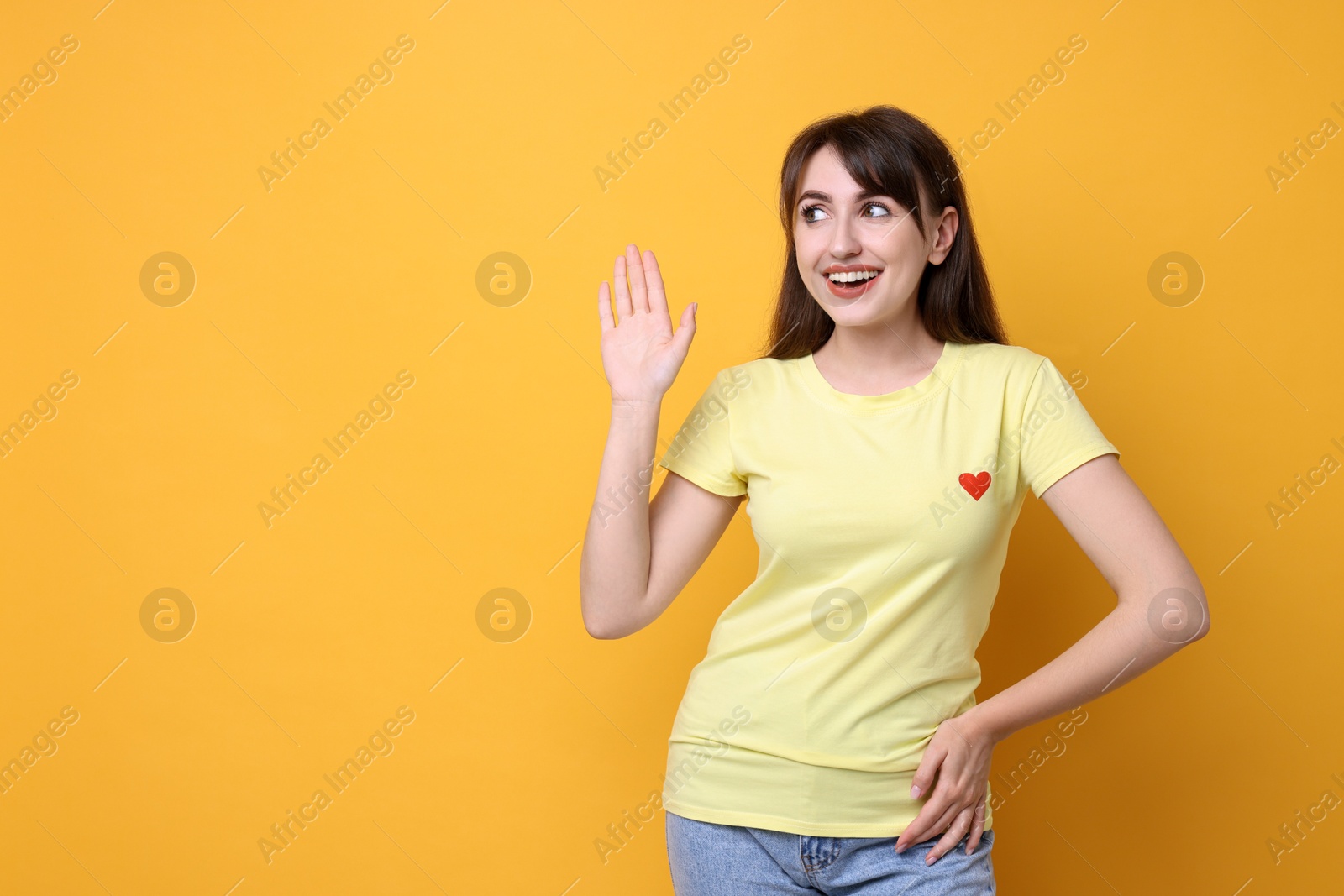 Photo of Happy young woman waving on orange background, space for text