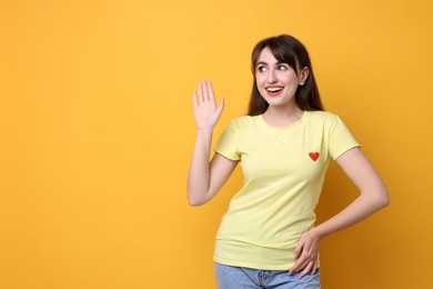 Happy young woman waving on orange background, space for text