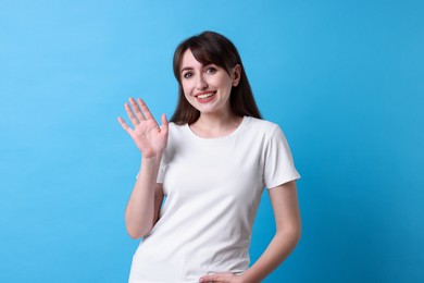 Photo of Happy woman waving on light blue background