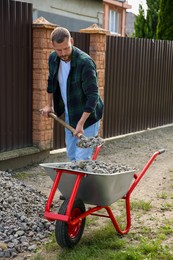 Man with shovel loading stones into wheelbarrow outdoors