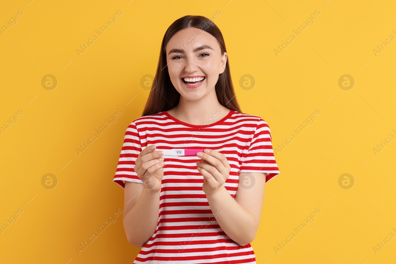 Photo of Happy woman holding pregnancy test on orange background