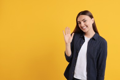 Happy young woman waving on orange background, space for text