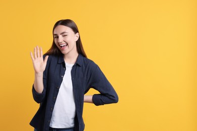 Happy young woman waving on orange background, space for text