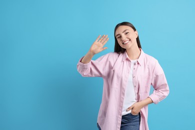 Photo of Happy woman waving on light blue background, space for text