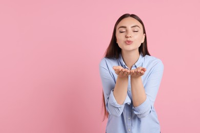 Beautiful woman blowing kiss on pink background, space for text